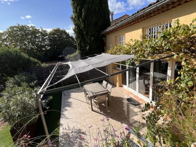 Terrasse intimiste Cette image présente la terrasse carrelée du gite Shelby, équipée d'une pergola en acier avec une toile d'ombrage grise, délimitée par des bacs en Corten avec des végétaux de type lauriers et méditerranéens. La terrasse comporte une table à manger et 6 fauteuils, ainsi que 4 fauteuils bas de jardin.