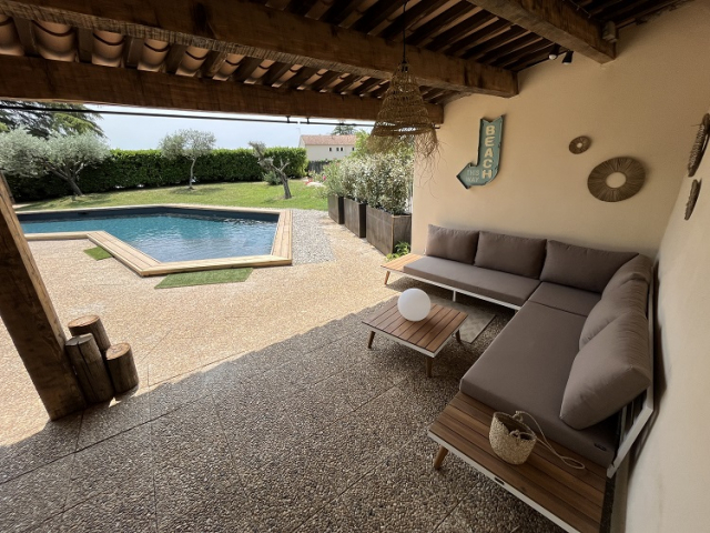l'espace salon détente du Pool House Cette image présente la piscine du Temps des Légendes vue depuis le Pool House. Elle est sécurisée par une clôture et arborée par des oliviers et une haie végétale.