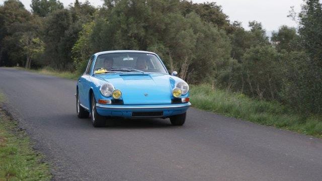 Cette image présente une Porsche 911 bleu sur une route des cévennes avec la garrigues en arrière plan