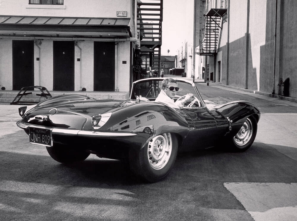 Cette image représente l'acteur Steve McQueen au volant d'une Jaguar XKSS dans les rues de Los Angeles