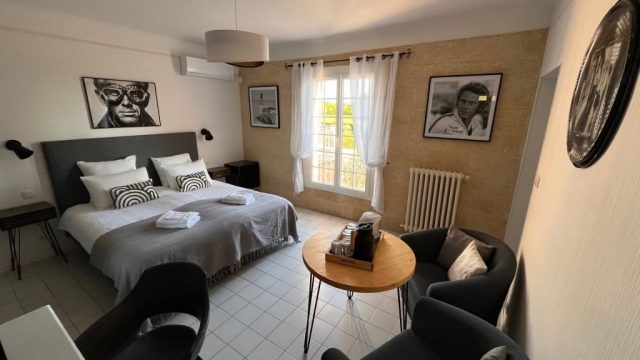 Cette image présente la chambre d'hôte Steve McQueen du Temps des Légendes. Elle est composée d'1 lit de 180 x 200 cm. La chambre est équipée d'une table, 2 fauteuils, d'un bureau avec fauteuil et d'un grand dressing.