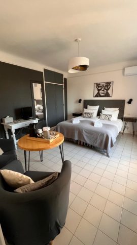 Cette image présente la chambre d'hôte Steve McQueen du Temps des Légendes. Elle est composée d'1 lit de 180 x 200 cm. La chambre est équipée d'une table, 2 fauteuils, d'un bureau avec fauteuil et d'un grand dressing.