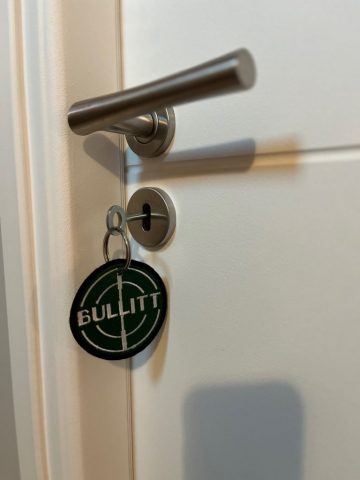 Cette image présente la clé de la chambre "Steve McQueen" à Le Temps Des Légendes, à l'effigie du célèbre film "Bullitt" et de la Mustang GT390 fastback éponyme