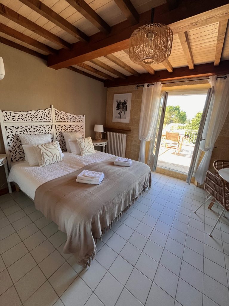 Cette image présente la chambre 1 de la chambre d'hôte Sean Connery du Temps des Légendes. Elle est composée d'1 lit de 180 x 200 cm. La chambre est équipée d'une table, 2 chaises et 2 fauteuils et d'un grand dressing. Elle donne accès à la terrasse privative.